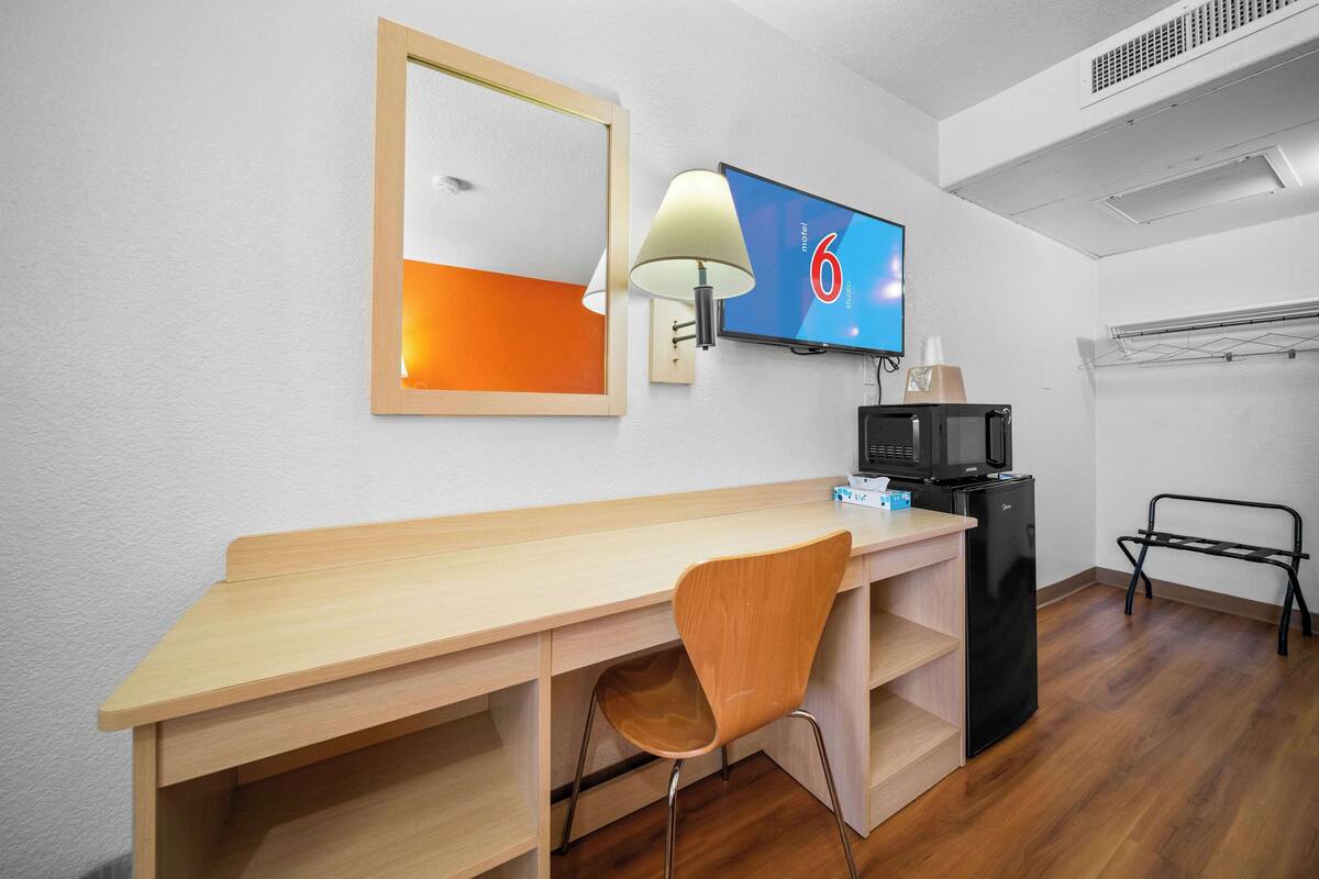 Een hotelkamer met een houten bureau, een stoel, een televisie, een magnetron en een minibar.
