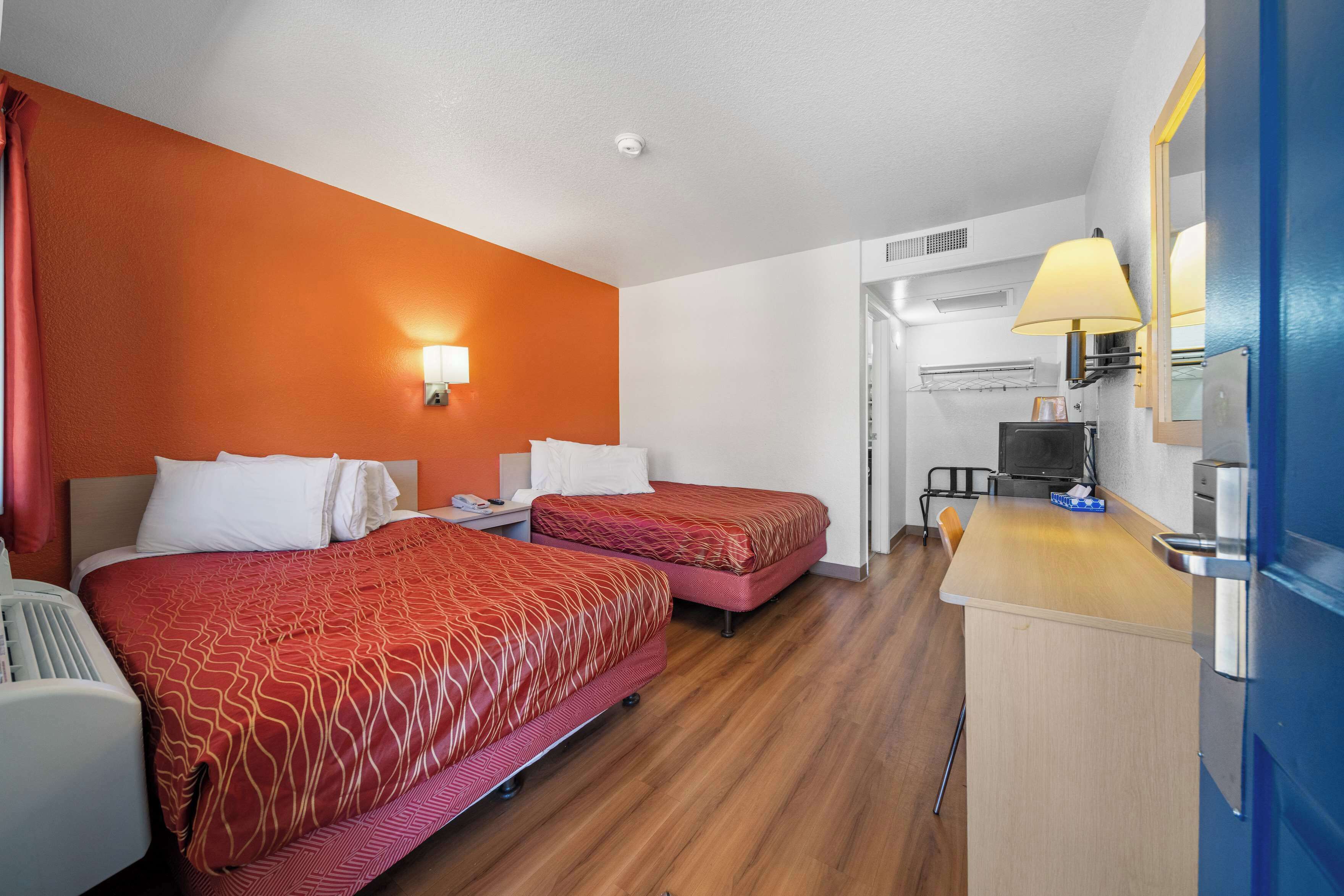 A hotel room with two beds, a small kitchenette, and a bathroom with a shower and toilet.