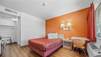 Habitación de hotel con cama, escritorio, silla y ventana con cortinas.
