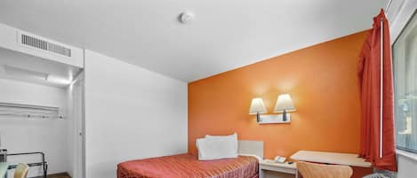 Habitación de hotel con cama, escritorio, silla y ventana con cortinas.