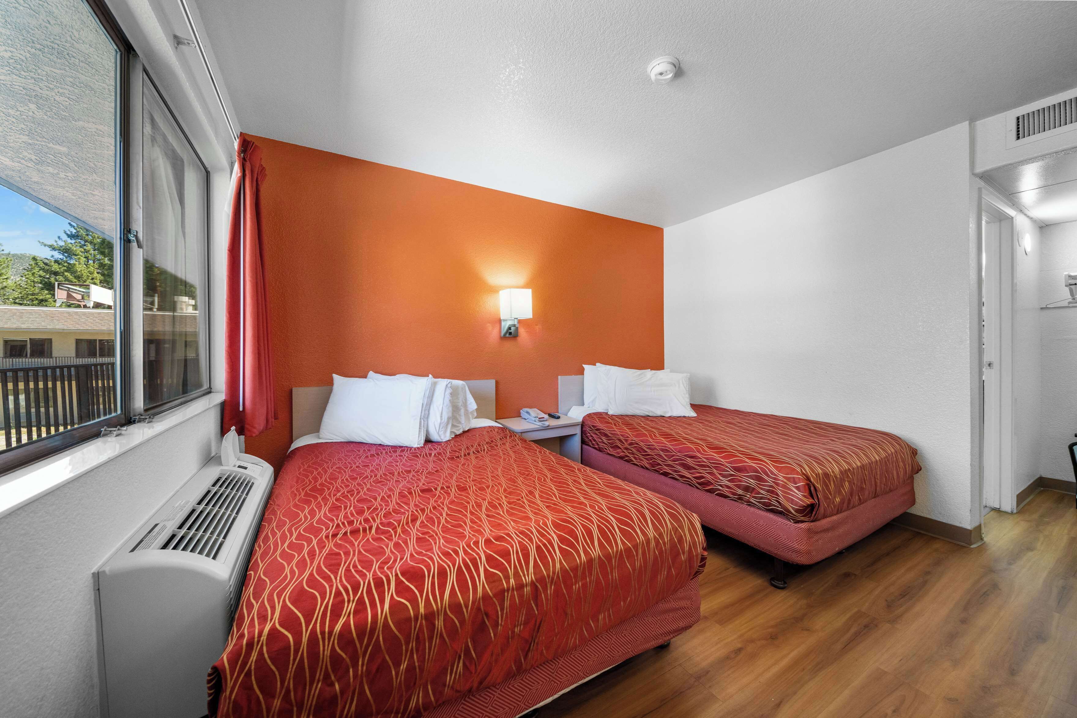 A hotel room with two beds, a window with blinds, a heater, and a wall-mounted light.