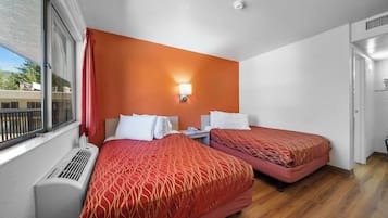 A hotel room with two beds, a window with blinds, a heater, and a wall-mounted light.