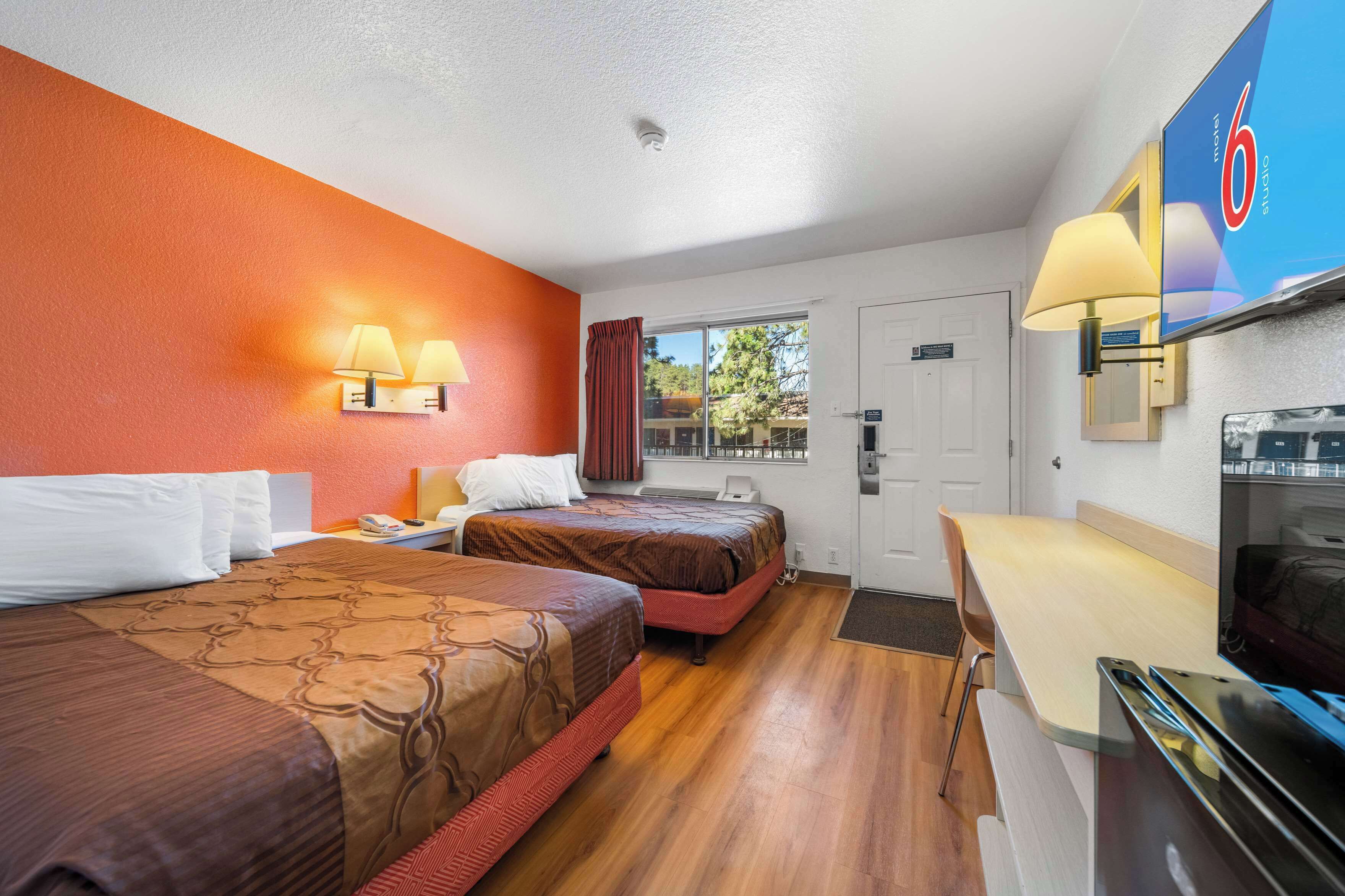 A hotel room with two beds, a desk, a TV, and a window with curtains.
