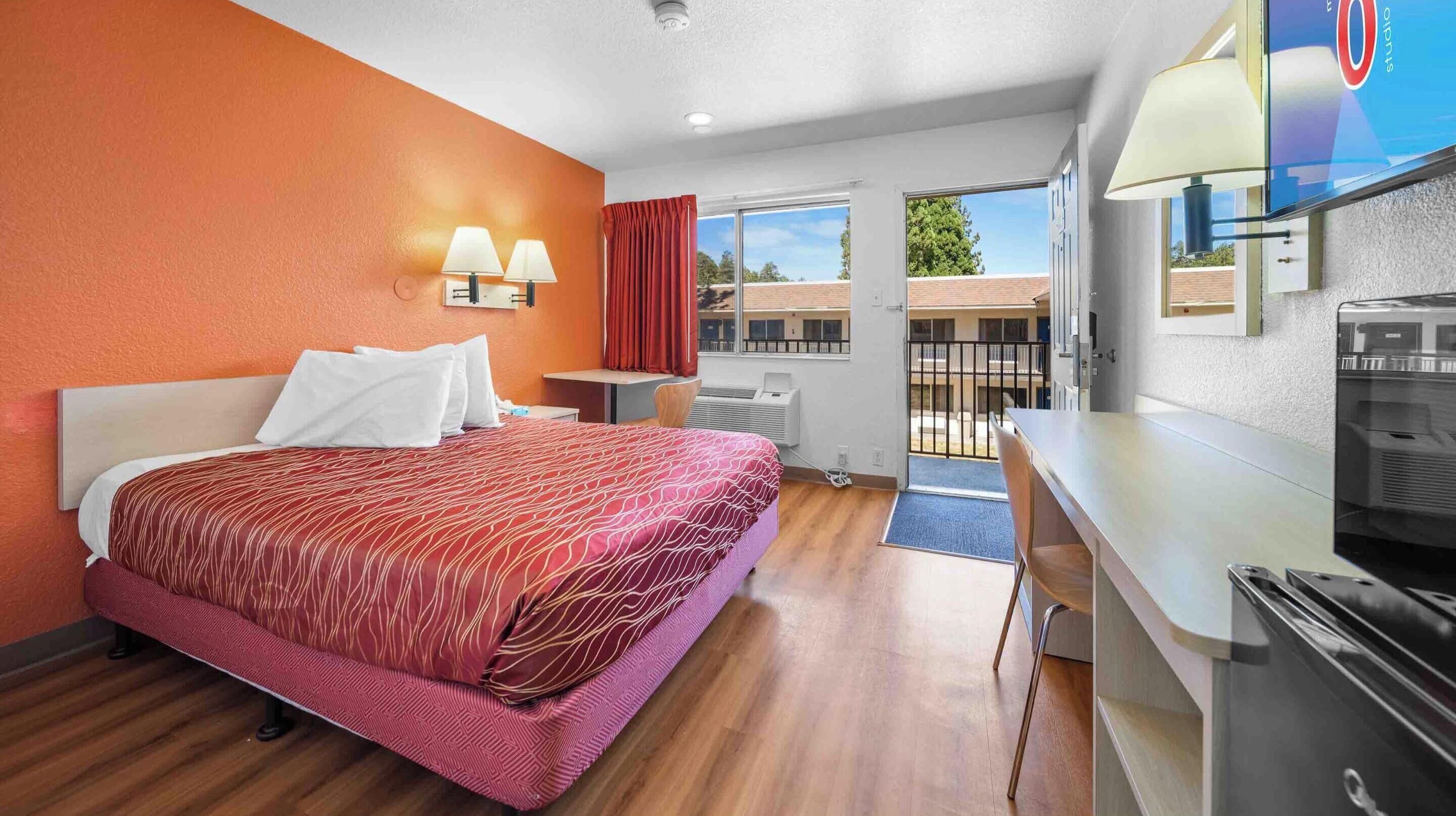A hotel room with a bed, a desk, a TV, and a window with a view of buildings.