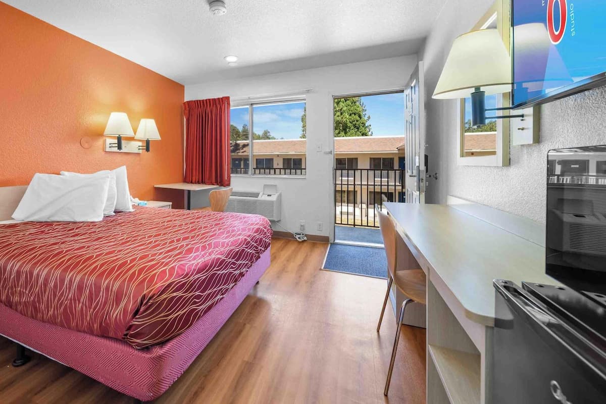 A hotel room with a bed, a desk, a TV, and a window with a view of buildings.