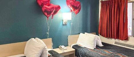 Habitación de hotel con dos camas, una mesita de noche con teléfono y globos en forma de corazón en la pared.