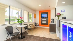 A hotel reception area with a modern design, including a reception desk, seating area, and a large window offering a view of the outdoors. - Motel 6 Carlsbad, CA Beach (Carlsbad)