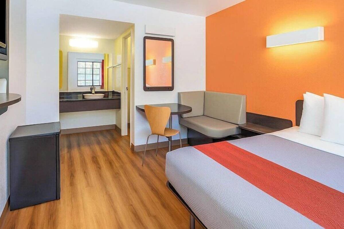 A hotel room with a bed, a desk, a chair, a small table, and a mirror.