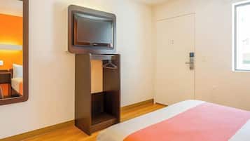 A hotel room with a bed, a TV mounted on a wooden stand, a wardrobe, and a door.