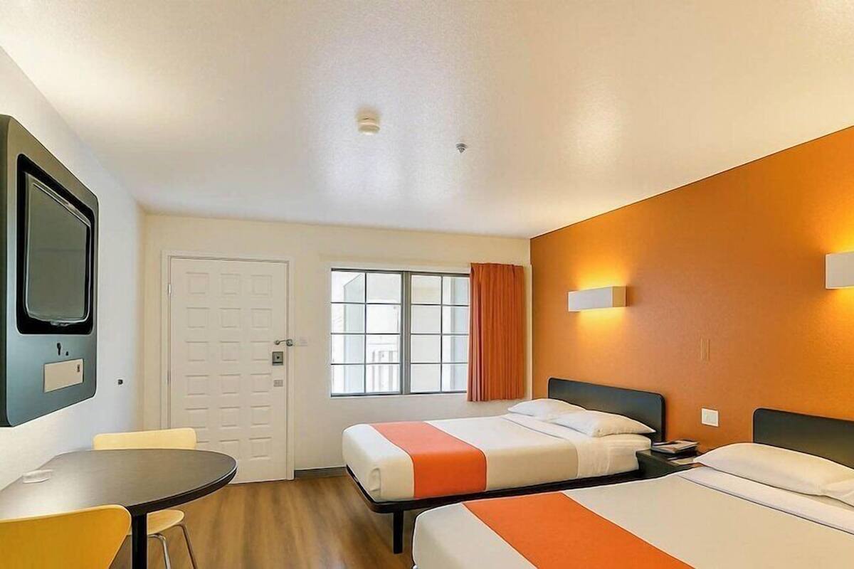 A hotel room with two beds, a desk, and a window with curtains.