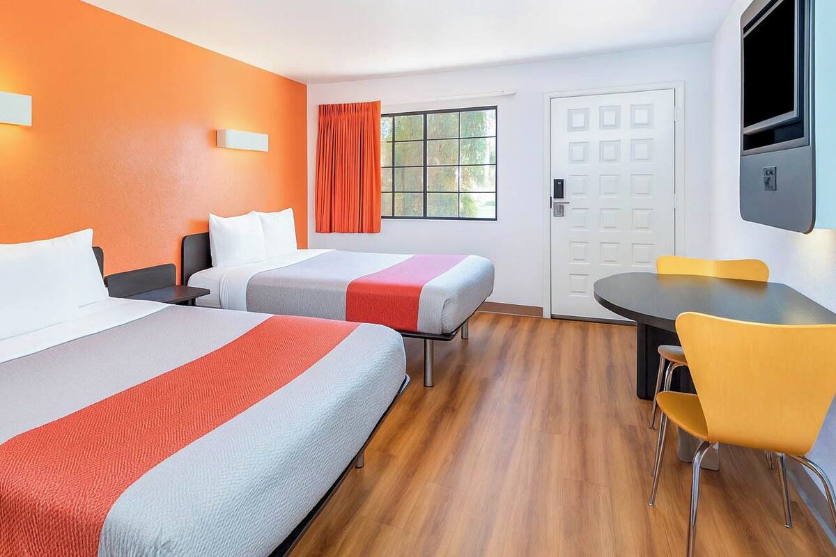 A hotel room with two beds, a dining table with yellow chairs, a TV, and a door.
