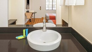 A bathroom with a round white sink, a mirror, and a window. - Motel 6 Carlsbad, CA Beach (Carlsbad)