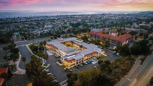 An aerial view of a hotel with multiple buildings, parking lots, and a surrounding urban area. - Motel 6 Carlsbad, CA Beach (Carlsbad)