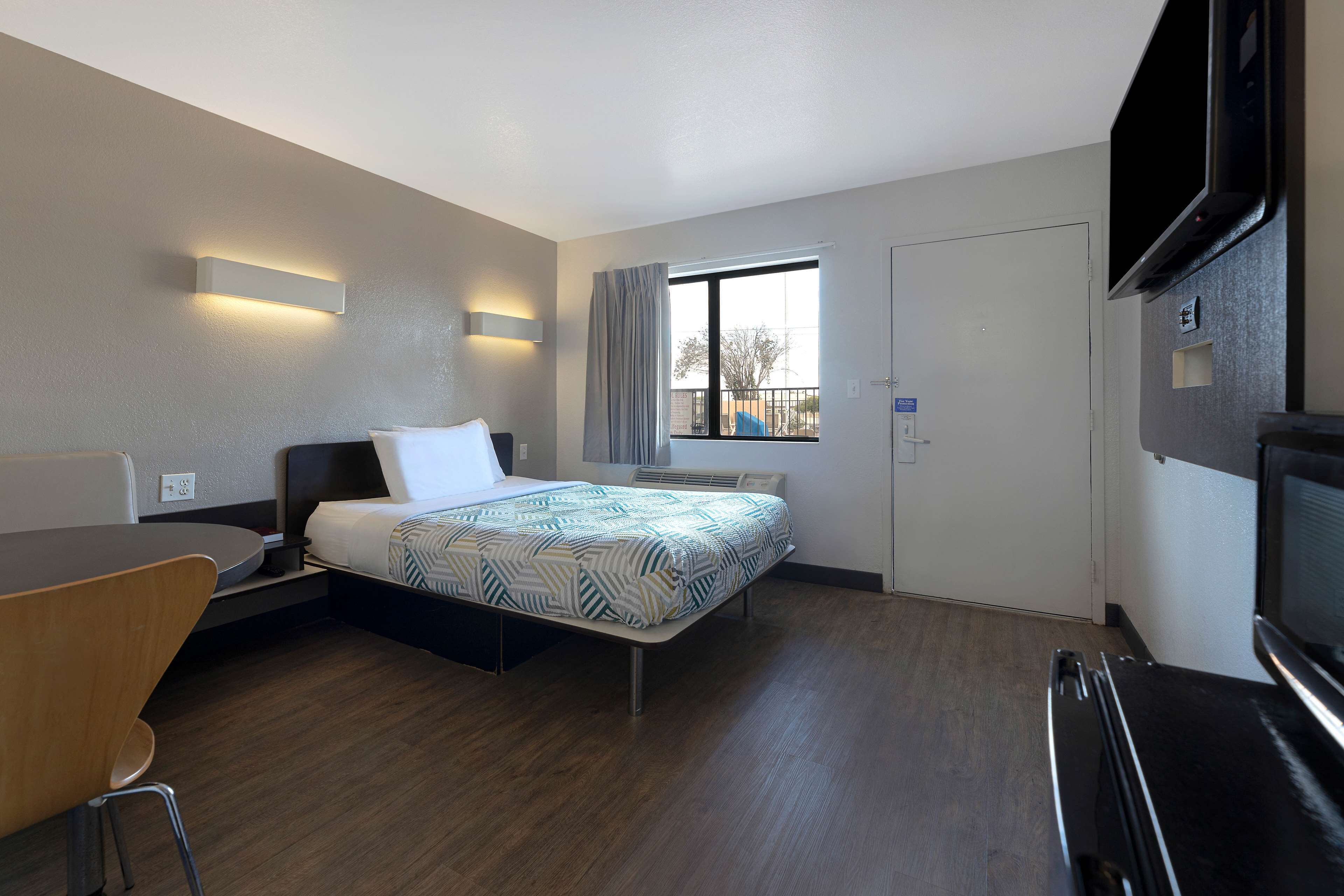 A hotel room with a bed, a desk, a chair, a TV, and a window with curtains.