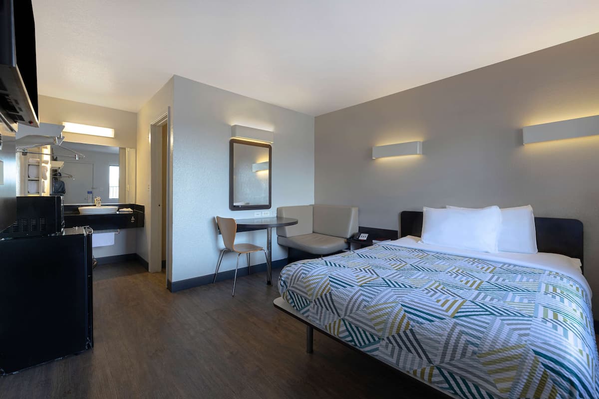 Ein Hotelzimmer mit Bett, Schreibtisch, Stuhl, Spiegel und einer Küchenzeile.