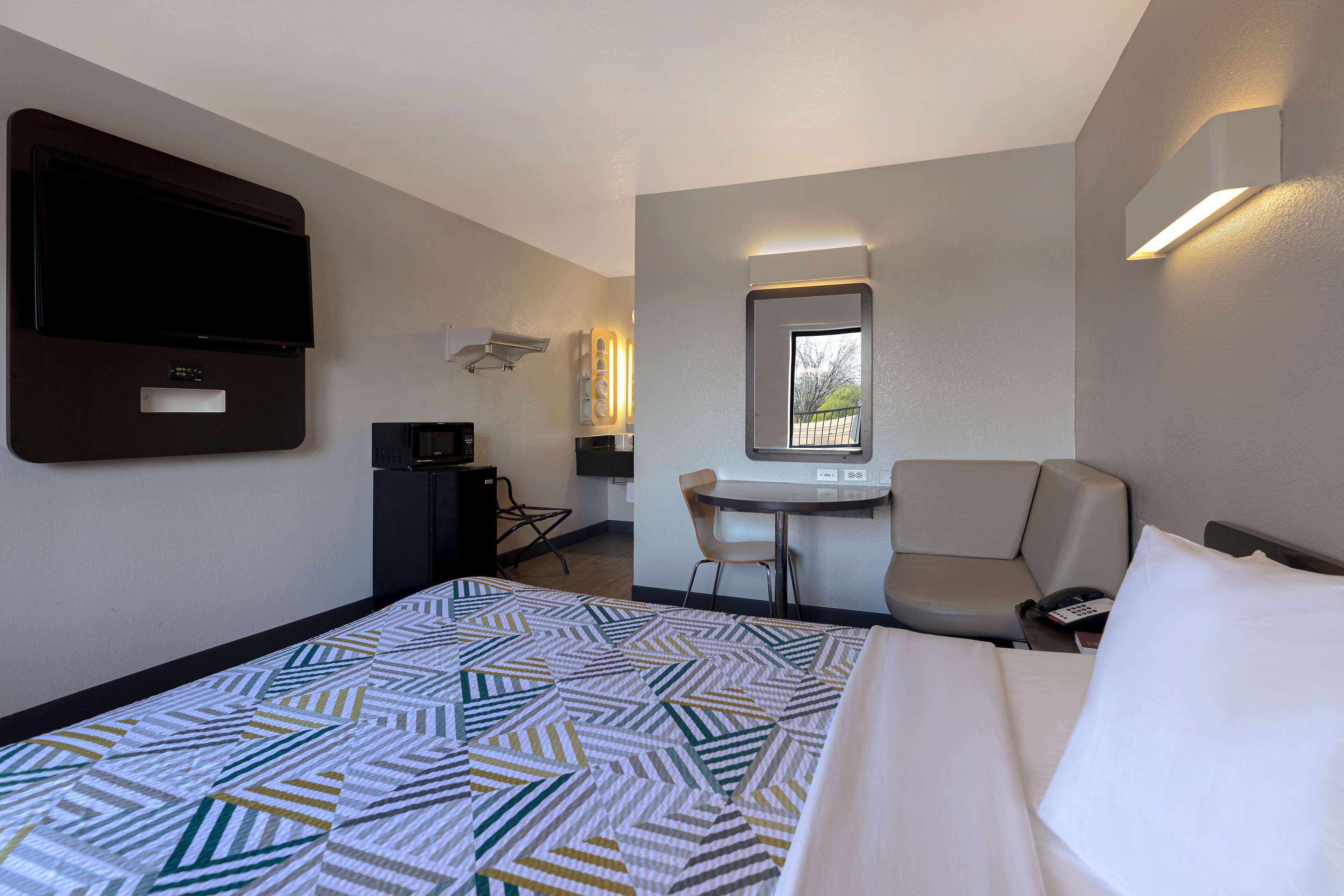 A hotel room with a bed, a desk, a chair, a TV, and a window.