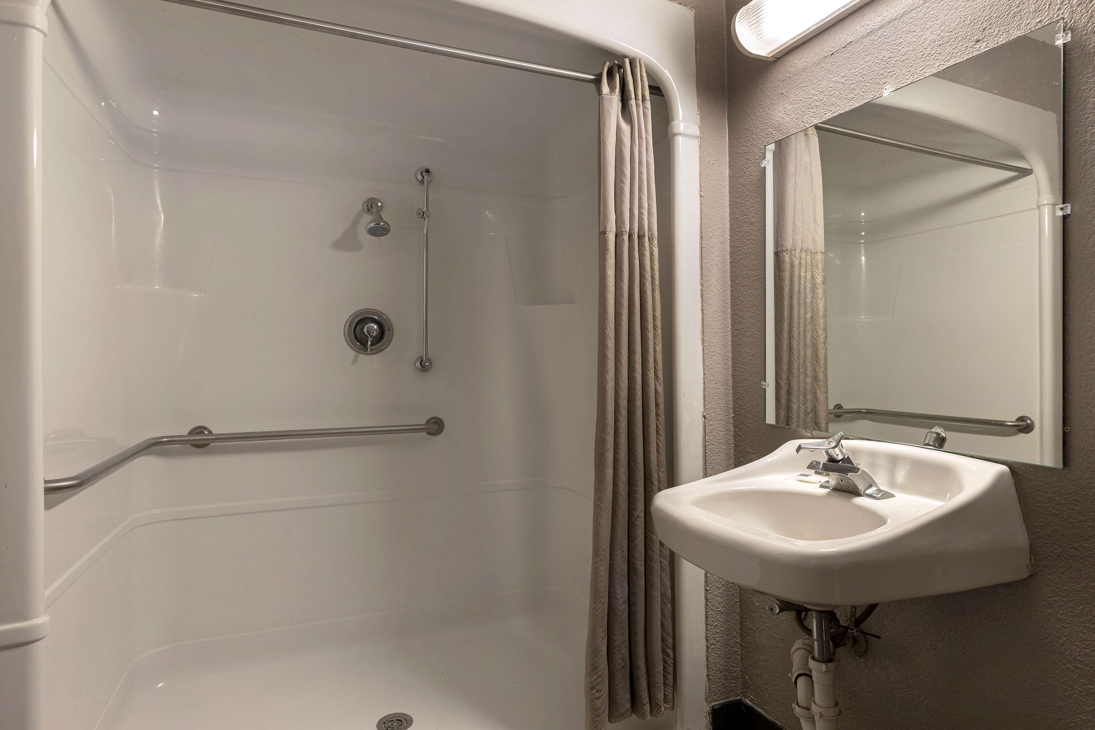 Une salle de bain équipée d’une douche à l’italienne, de barres d’appui, d’un lavabo et d’un miroir.