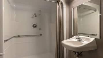 Une salle de bain équipée d’une douche à l’italienne, de barres d’appui, d’un lavabo et d’un miroir.