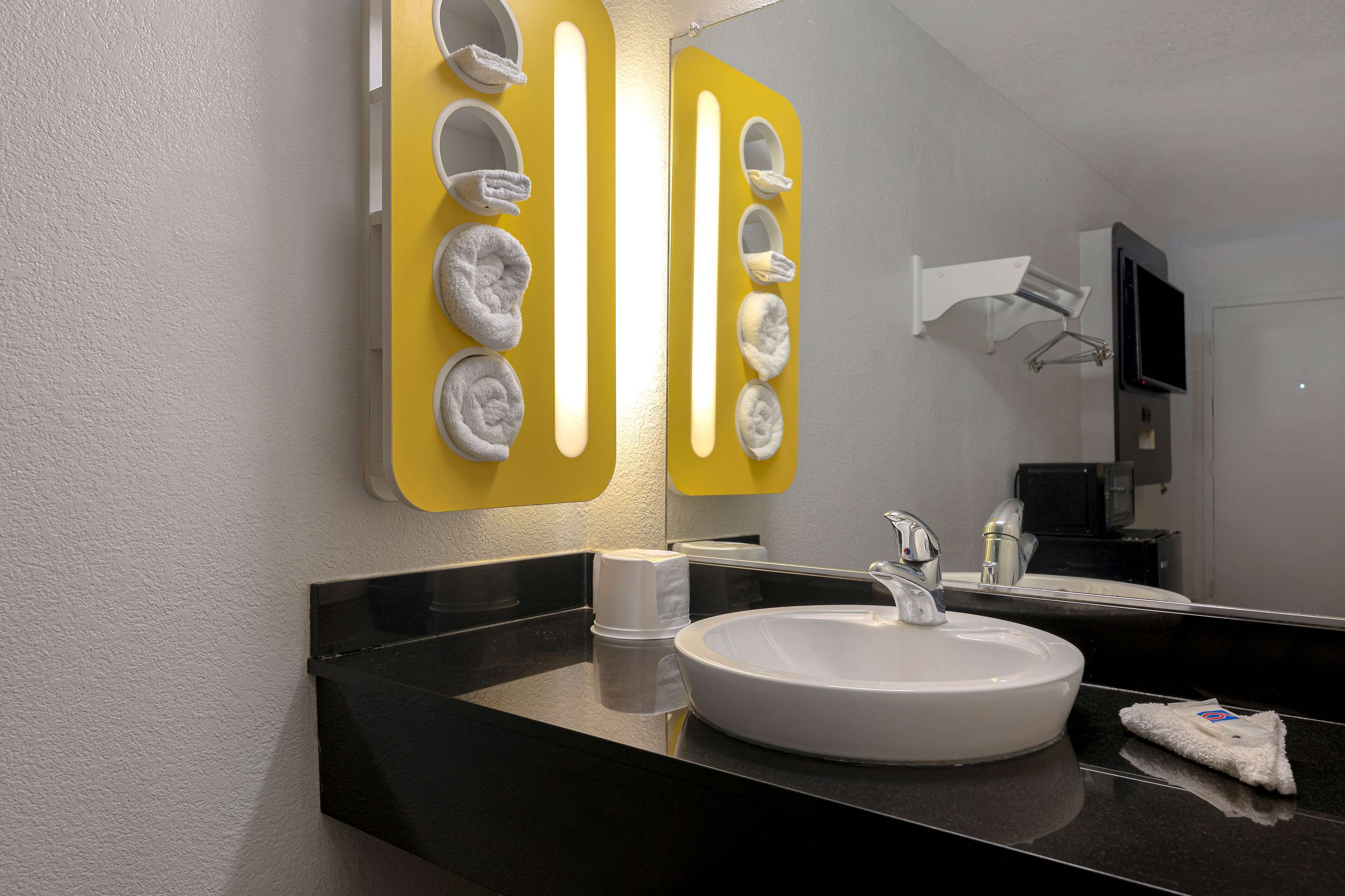 Un baño moderno con encimera negra, lavamanos blanco y espejo con sujetatelas amarillos.