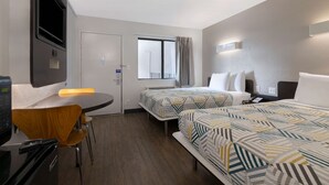 Une chambre d’hôtel avec deux lits, un bureau, une chaise, une télévision et une fenêtre avec des rideaux.