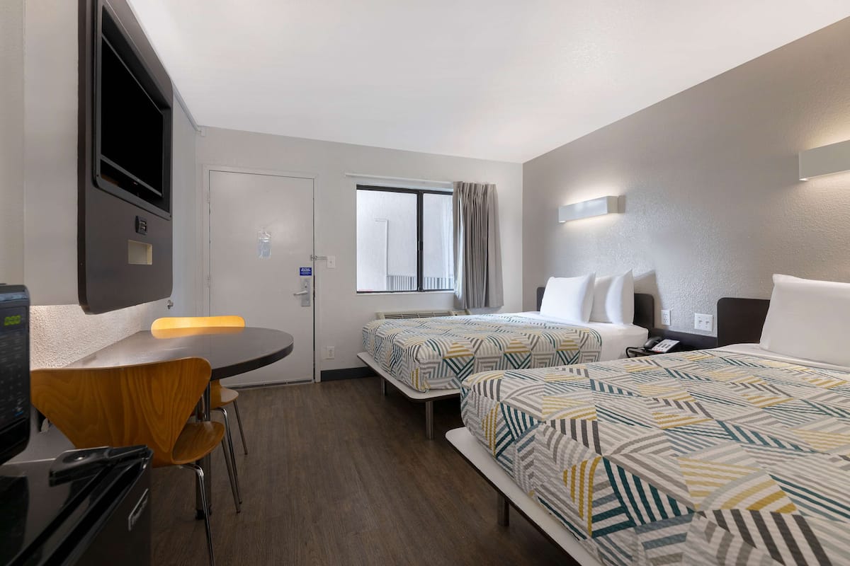 Ein Hotelzimmer mit zwei Betten, einem Schreibtisch, einem Stuhl, einem Fernseher und einem Fenster mit Vorhängen.