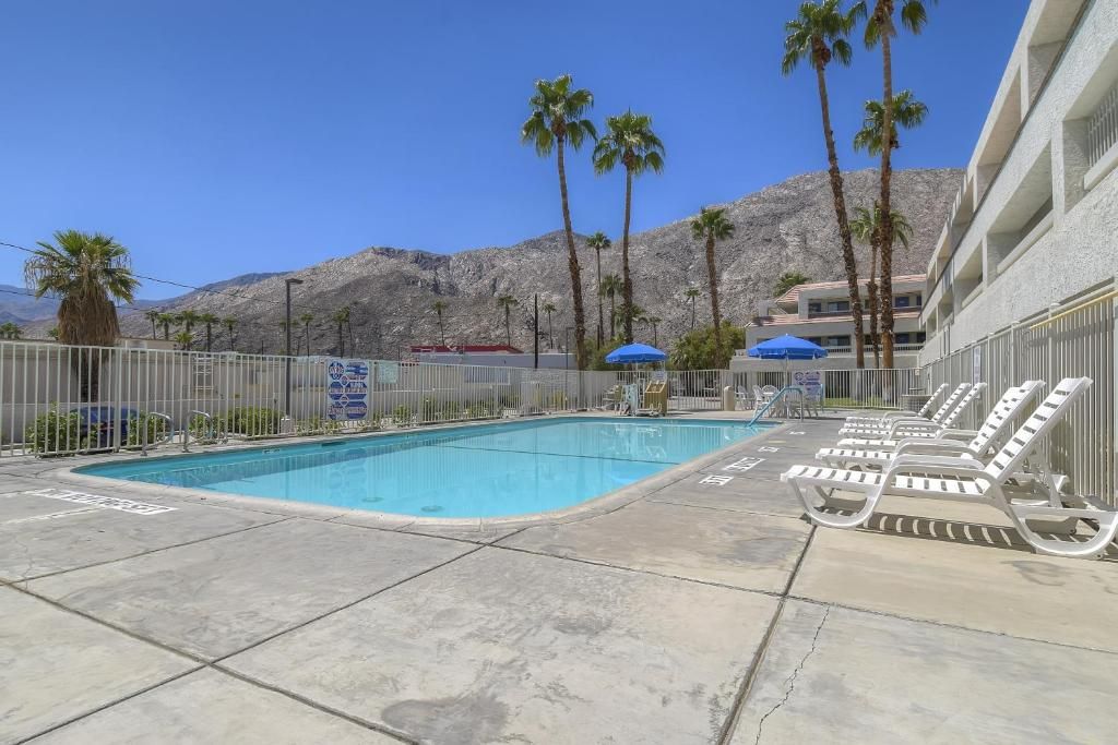 A swimming pool with lounge chairs and umbrellas, surrounded by palm trees and mountains.