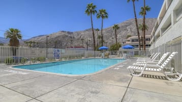 Une piscine entourée de palmiers et de montagnes, avec des chaises longues et des parasols.