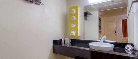 Uma casa de banho com bancada preta, lavatório branco e espelho. Toalhas penduradas num suporte e toalheiro amarelo.
