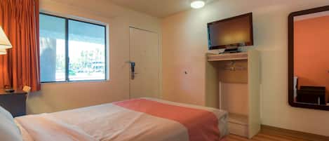 Una habitación de hotel con cama, televisor en la pared, ventana con cortinas y puerta.