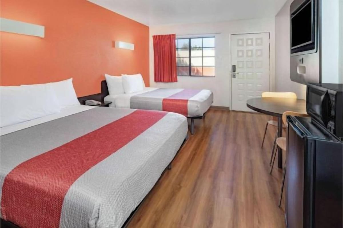 A hotel room with two beds, a TV, a small table, and a door.