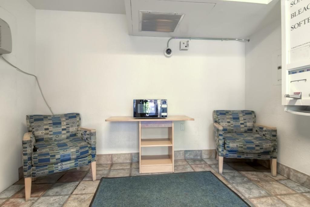 Una habitación con dos sillones estampados, una mesita de madera con un microondas y una alfombra azul.