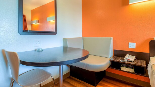 Une chambre d’hôtel avec une table ronde, un banc rembourré, une table de chevet avec un téléphone et un miroir au mur.