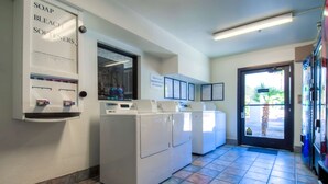 Une laverie équipée de machines à laver et de sèche-linge, d’un distributeur de savon et d’eau de Javel, ainsi que de panneaux d’information.