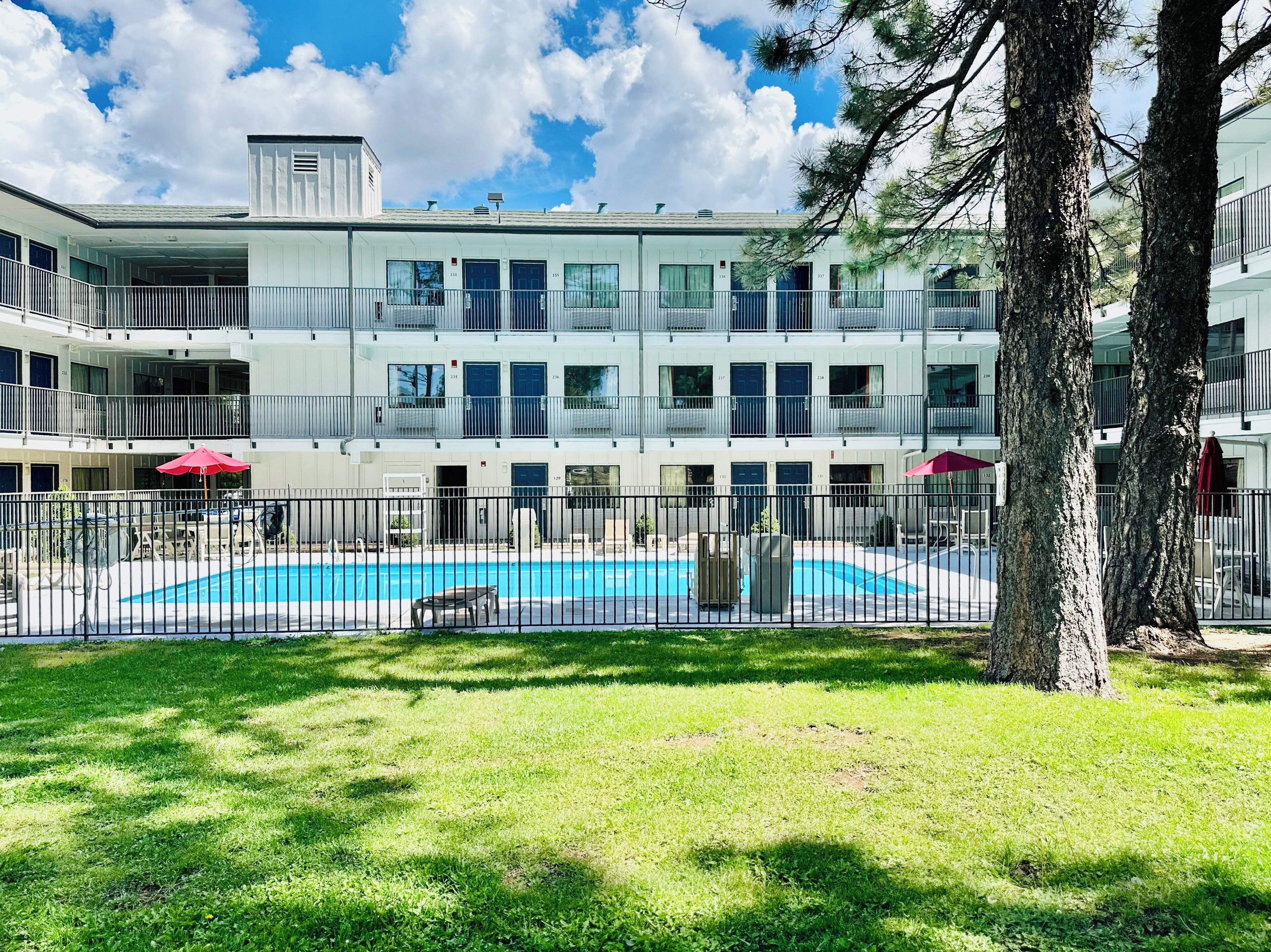 Un edificio de varios pisos con piscina, rodeado por una zona vallada y árboles.