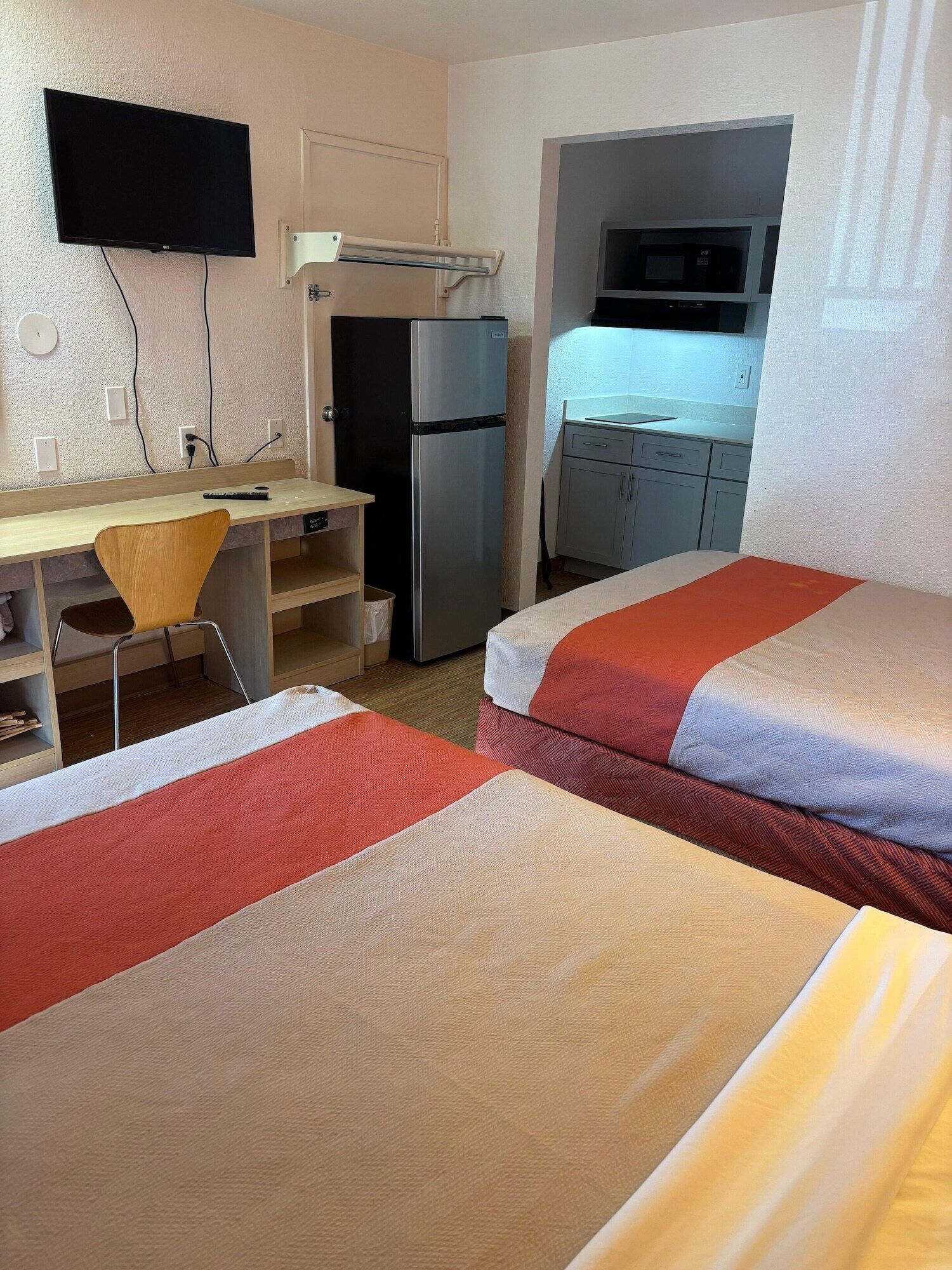 Une chambre d’hôtel avec deux lits, un bureau, une chaise, un réfrigérateur et un téléviseur fixé au mur.