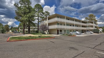 A multi-story building with balconies, a parking lot, and surrounding trees.