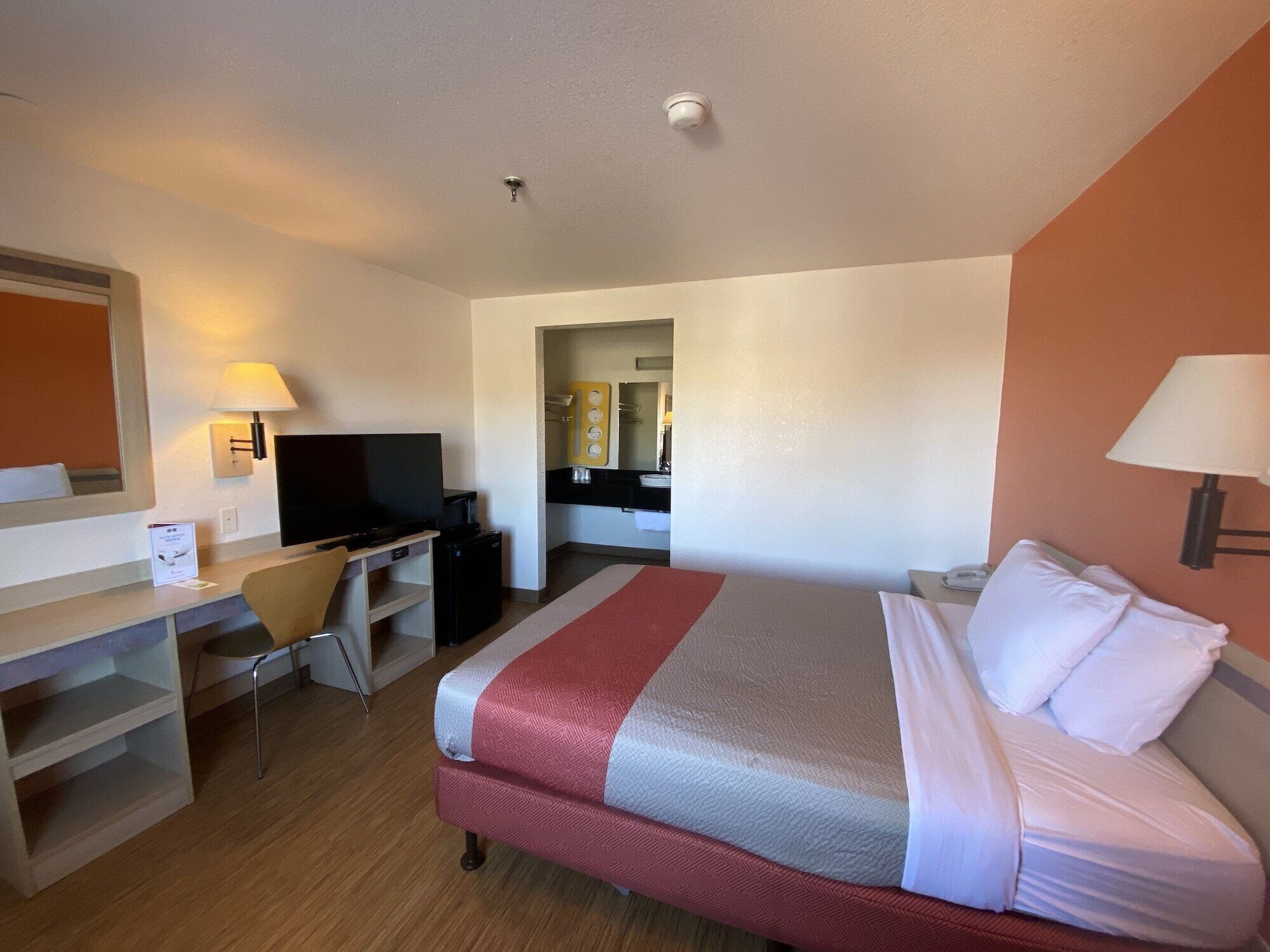 A hotel room with a bed, a desk with a television, a chair, and a mirror.