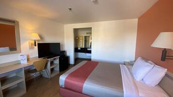 A hotel room with a bed, a desk with a television, a chair, and a mirror.