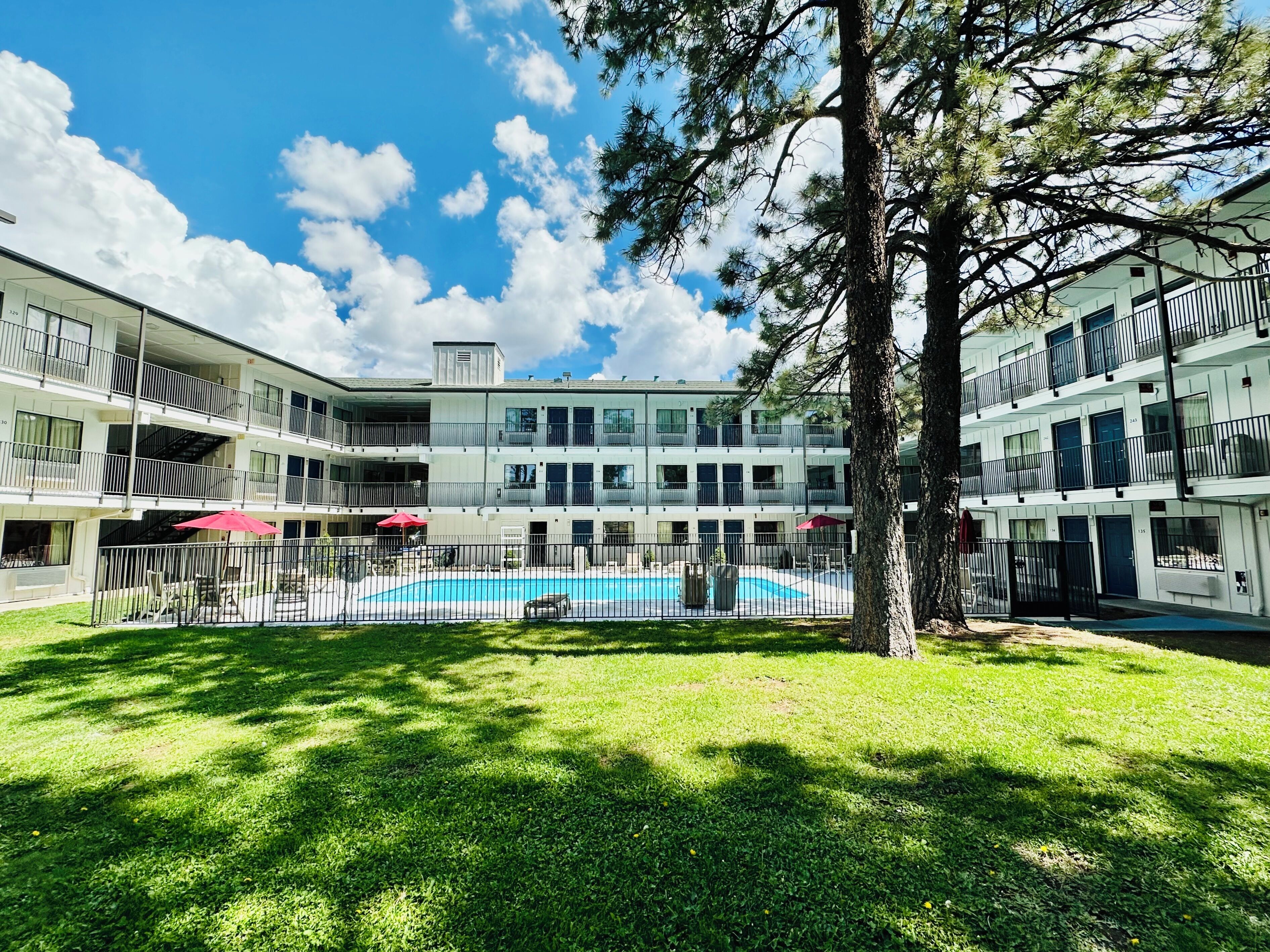 A multi-story building with a swimming pool surrounded by a fenced area and a tree.