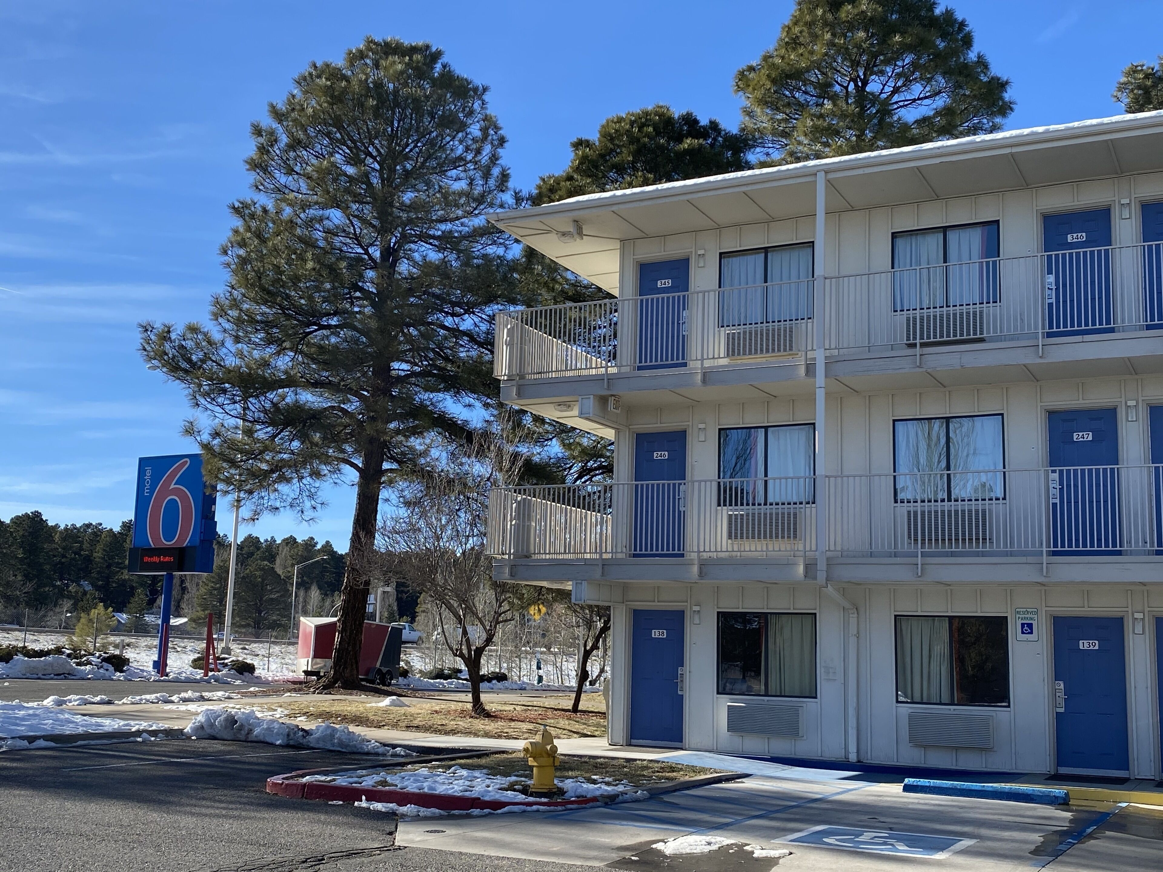 A motel with a blue and white exterior, multiple balconies, and a parking area with snow.