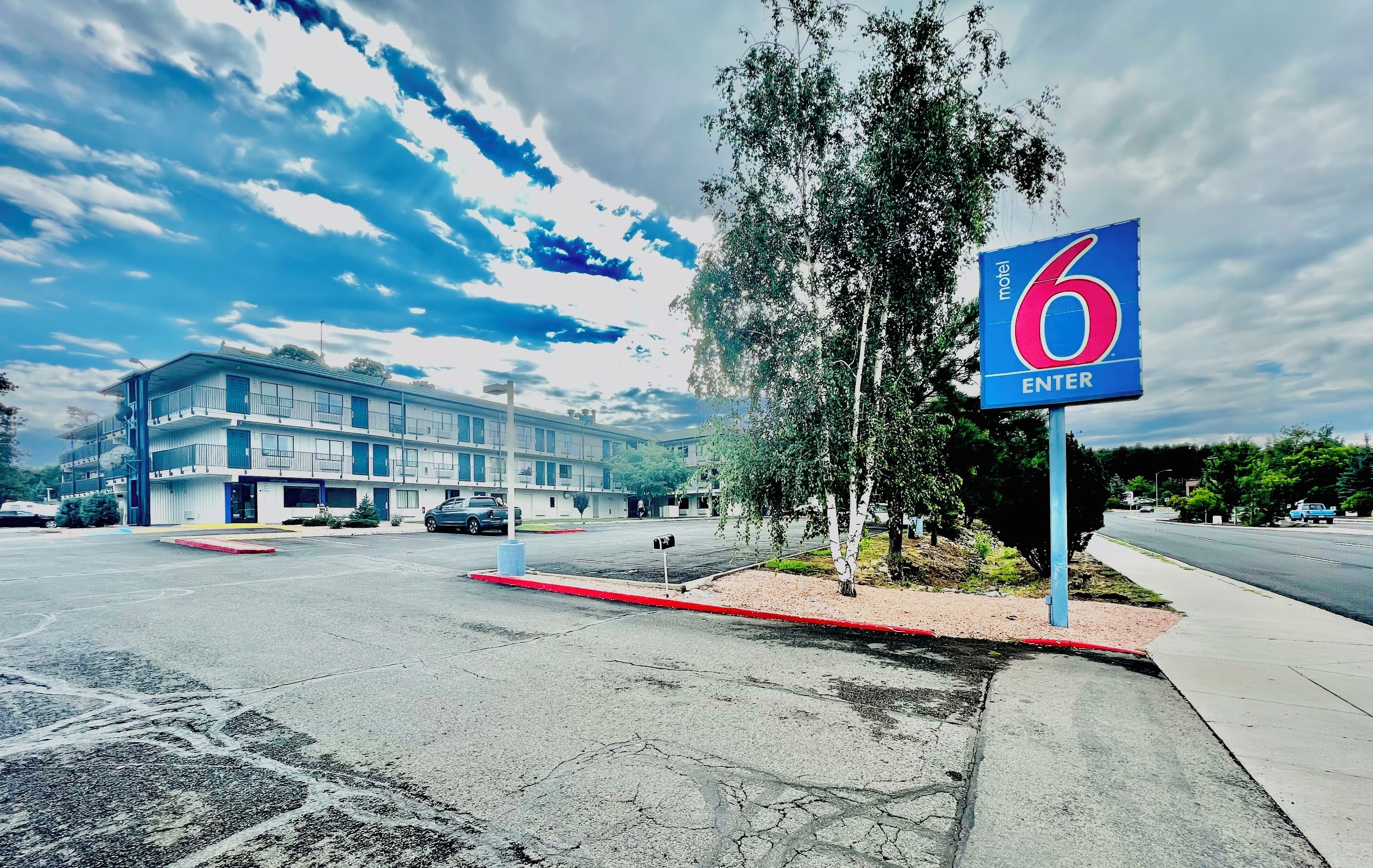 Une enseigne de motel avec le chiffre 6 et le symbole « ENTRÉE », un bâtiment en arrière-plan, un parking et un trottoir.