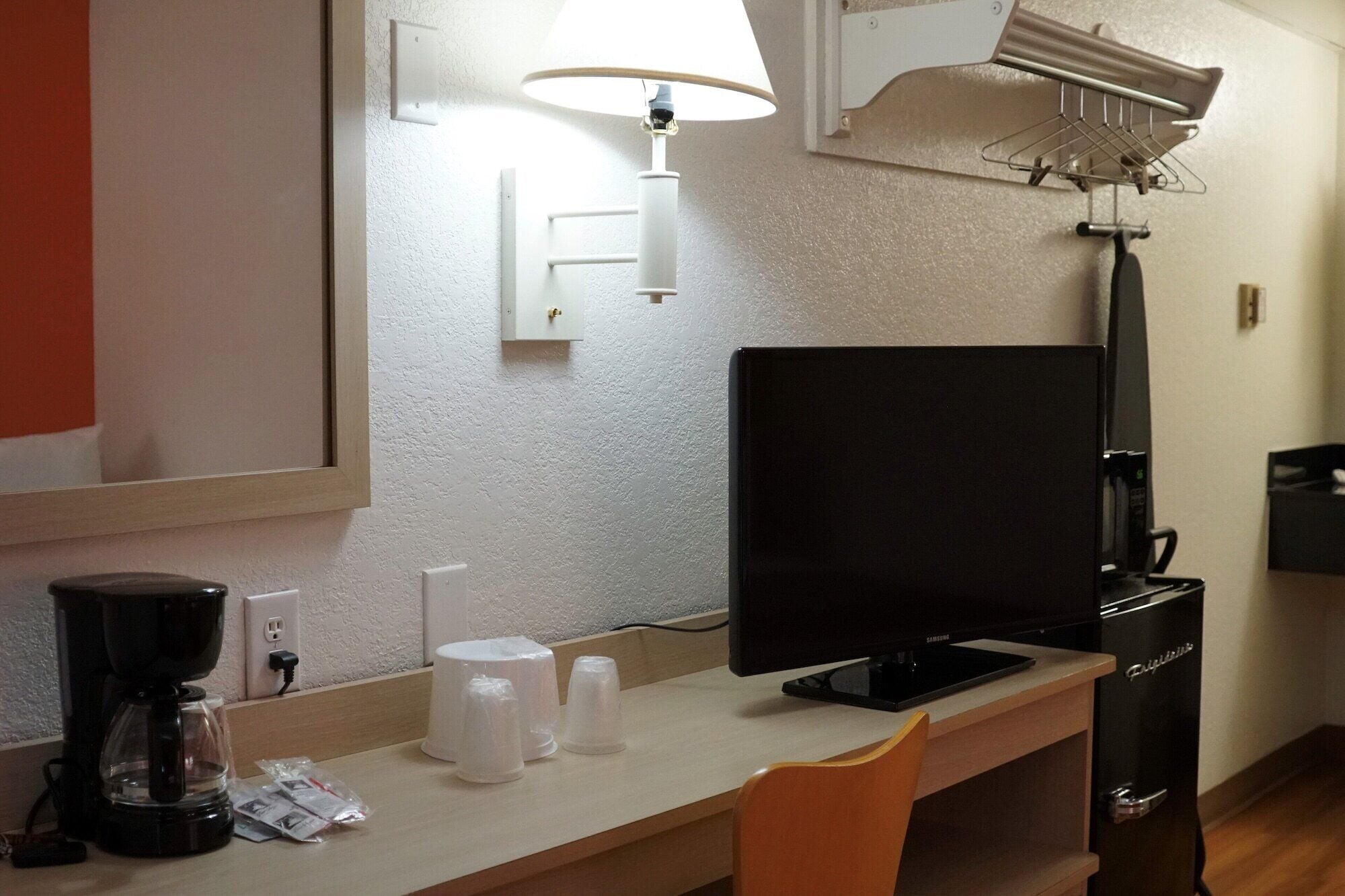 A hotel room with a desk, a flat-screen TV, a coffee maker, and a refrigerator.