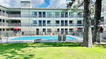 Un edificio de varios pisos con piscina, rodeado por un área cercada y árboles.