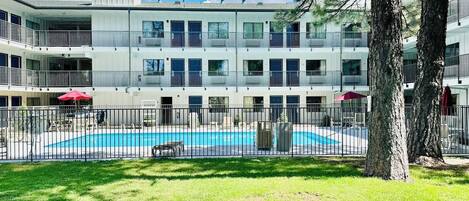 Un edificio de varios pisos con piscina, rodeado por un área cercada y árboles.