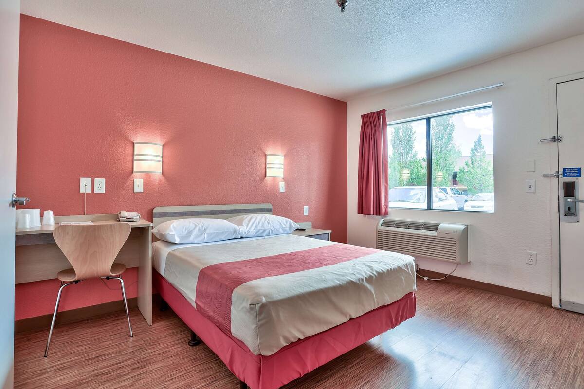 Une chambre d’hôtel avec un lit, un bureau, une chaise et une fenêtre avec des rideaux.