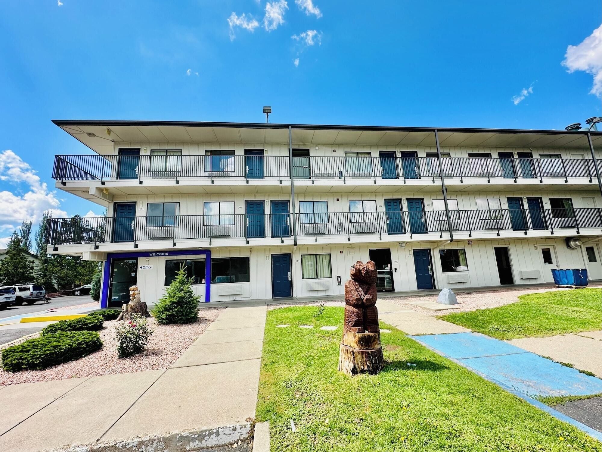 A two-story motel with a flat roof, multiple balconies, and a parking lot in front.