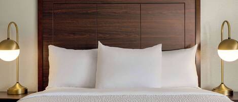 Cama bem arrumada com lençóis brancos e duas luminárias de cabeceira.