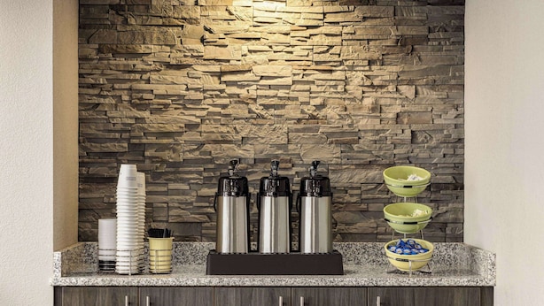 Cozinha com painel de pedra, estação de café com dispensadores e um buffet com tigelas e copos.
