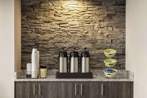 A kitchen area with a stone backsplash, a coffee station with dispensers, and a buffet setup with bowls and cups. - AmericInn by Wyndham Madison WI (Madison)