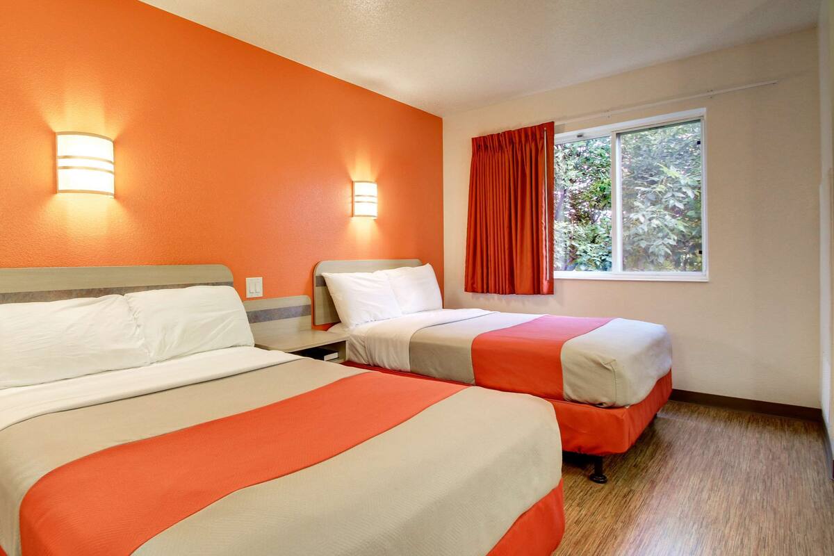 A hotel room with two beds, orange walls, and a window with red curtains.
